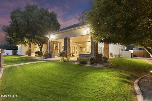 view of front of house featuring a lawn, a patio area, fence, and stucco siding