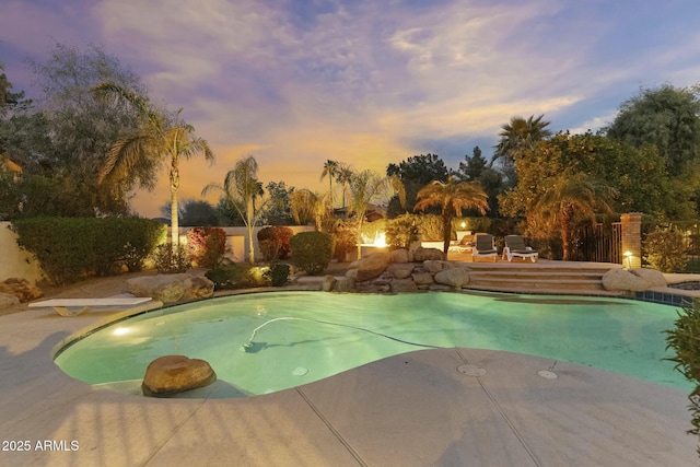 pool at dusk featuring a diving board, a fenced in pool, and a patio