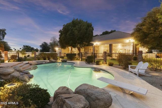 pool at dusk with a fenced in pool, fence, a patio, and a diving board