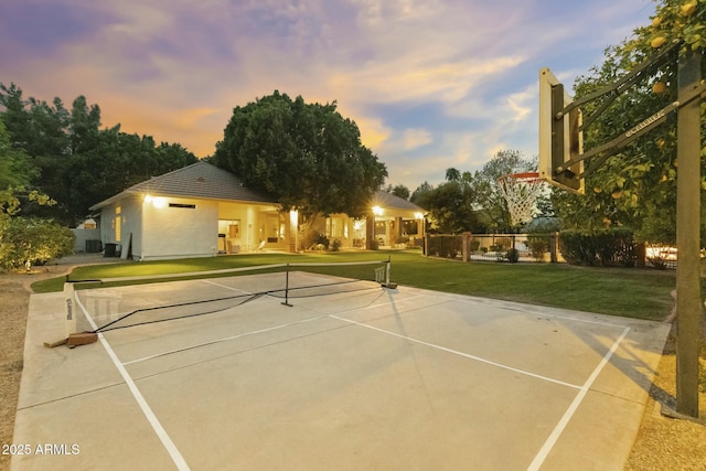 view of tennis court featuring community basketball court, fence, and a lawn