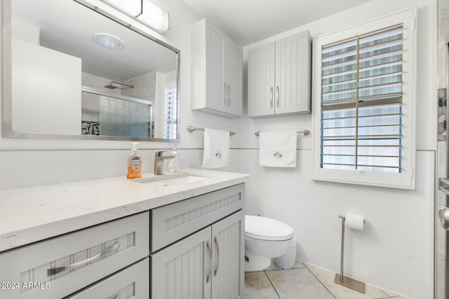 bathroom featuring tile patterned flooring, toilet, vanity, a shower with shower door, and tile walls