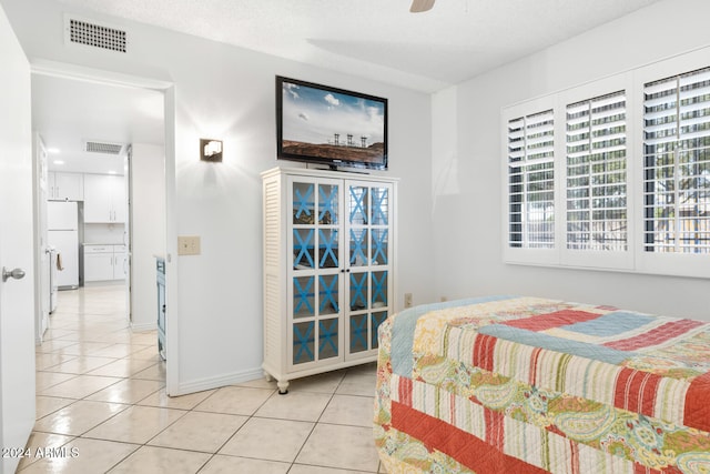 bedroom featuring ensuite bathroom, white refrigerator, ceiling fan, light tile patterned floors, and a textured ceiling