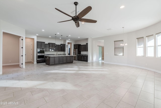 unfurnished living room featuring light tile patterned floors, sink, and ceiling fan with notable chandelier