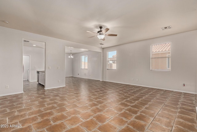 tiled empty room with ceiling fan with notable chandelier