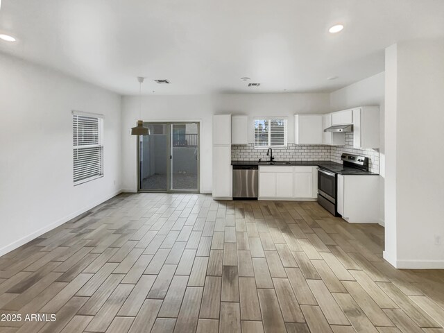 kitchen featuring dark countertops, appliances with stainless steel finishes, hanging light fixtures, white cabinetry, and a sink
