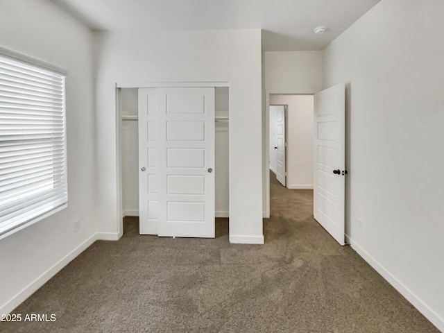 unfurnished bedroom with baseboards, dark colored carpet, and a closet