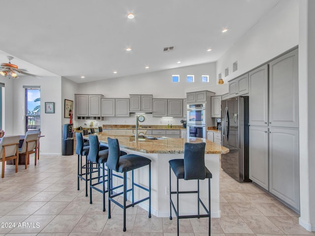 kitchen with ceiling fan, an island with sink, lofted ceiling, appliances with stainless steel finishes, and light stone countertops