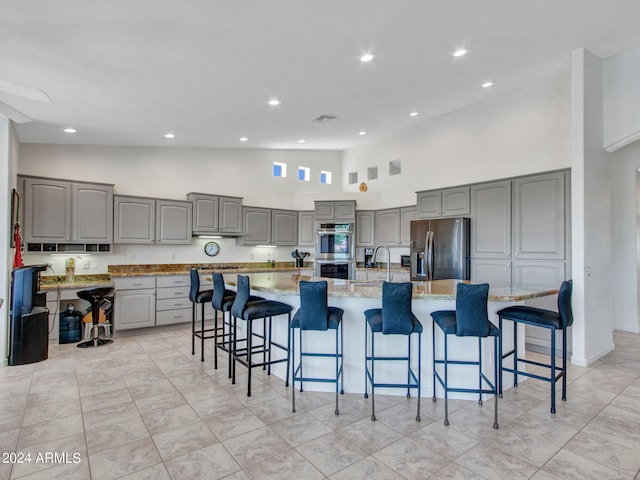 kitchen with a spacious island, gray cabinets, appliances with stainless steel finishes, and a kitchen bar