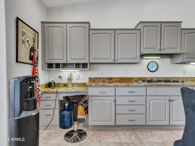 kitchen with stainless steel gas stovetop, lofted ceiling, light tile patterned floors, and gray cabinetry