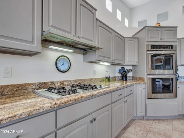 kitchen with gray cabinetry, white gas cooktop, light stone countertops, light tile patterned floors, and stainless steel double oven