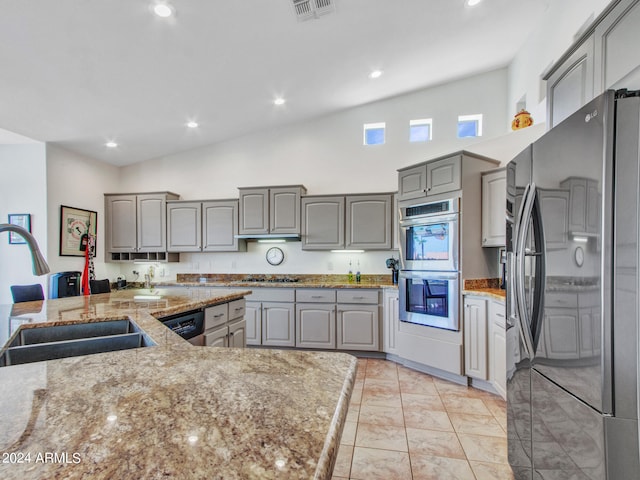 kitchen featuring appliances with stainless steel finishes, gray cabinetry, light stone countertops, lofted ceiling, and sink