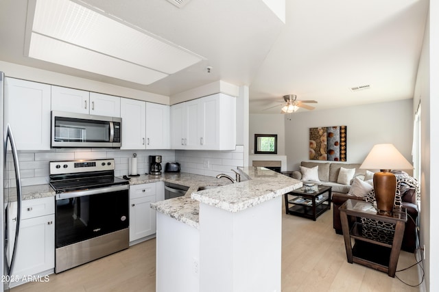 kitchen with appliances with stainless steel finishes, a peninsula, light wood-style flooring, a sink, and tasteful backsplash