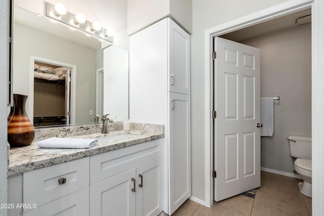 bathroom featuring tile patterned floors, toilet, vanity, baseboards, and a spacious closet
