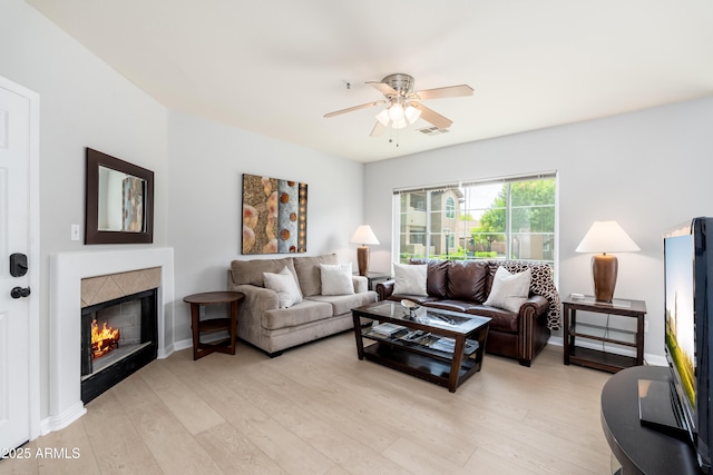 living area featuring a ceiling fan, light wood-style floors, a tiled fireplace, and baseboards