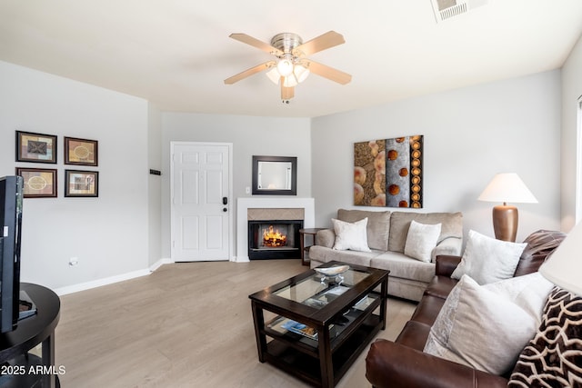 living area with a ceiling fan, light wood finished floors, a lit fireplace, and baseboards