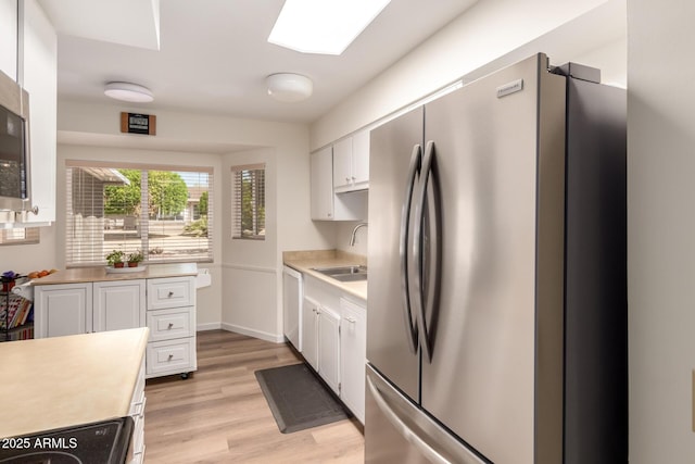 kitchen featuring a sink, freestanding refrigerator, light wood-style floors, white cabinetry, and light countertops