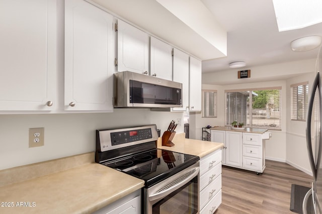 kitchen with light wood-type flooring, light countertops, white cabinetry, and stainless steel appliances