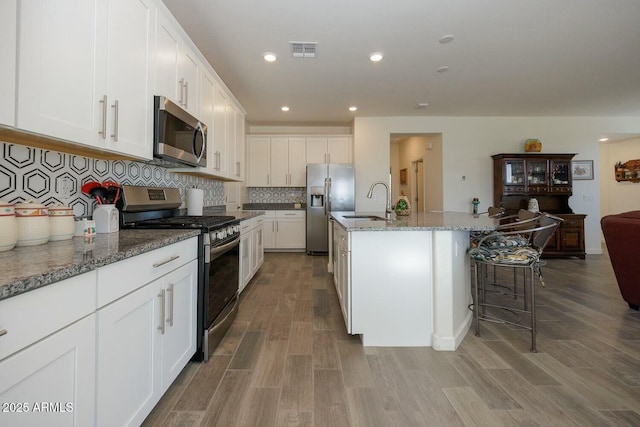 kitchen featuring tasteful backsplash, light stone counters, stainless steel appliances, white cabinets, and an island with sink