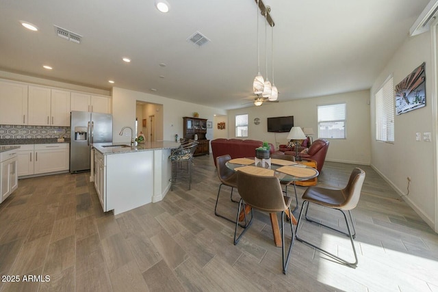 kitchen with pendant lighting, sink, ceiling fan, an island with sink, and stainless steel fridge with ice dispenser