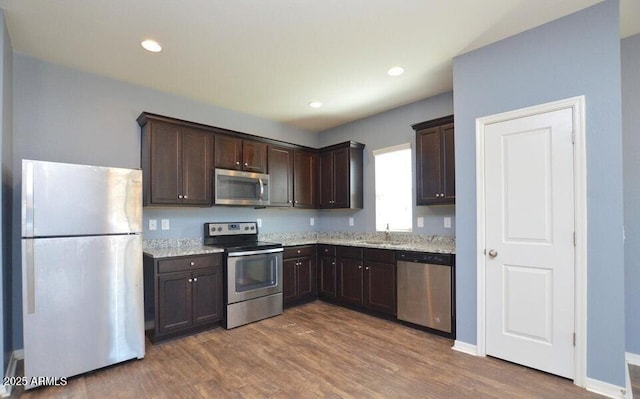 kitchen with light stone counters, appliances with stainless steel finishes, dark hardwood / wood-style flooring, and sink