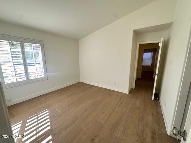 spare room featuring wood-type flooring and vaulted ceiling