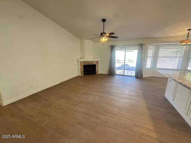 unfurnished living room featuring ceiling fan with notable chandelier, dark hardwood / wood-style flooring, and a fireplace