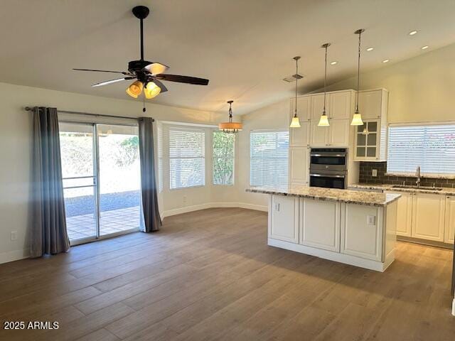 kitchen featuring light stone countertops, a center island, decorative light fixtures, white cabinetry, and double oven