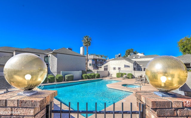 community pool featuring a patio area, fence, a residential view, and a hot tub