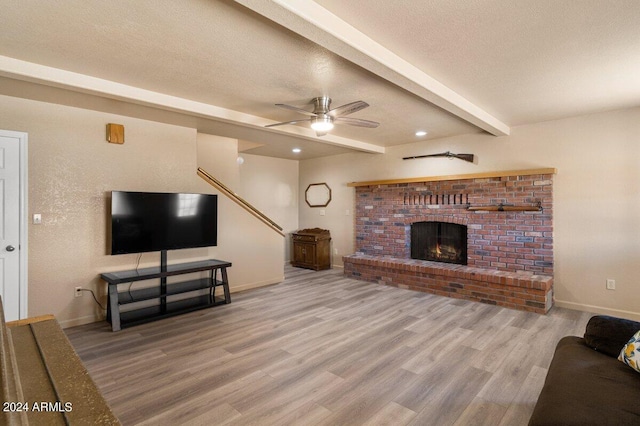 living room featuring a brick fireplace, ceiling fan, a textured ceiling, beam ceiling, and wood-type flooring