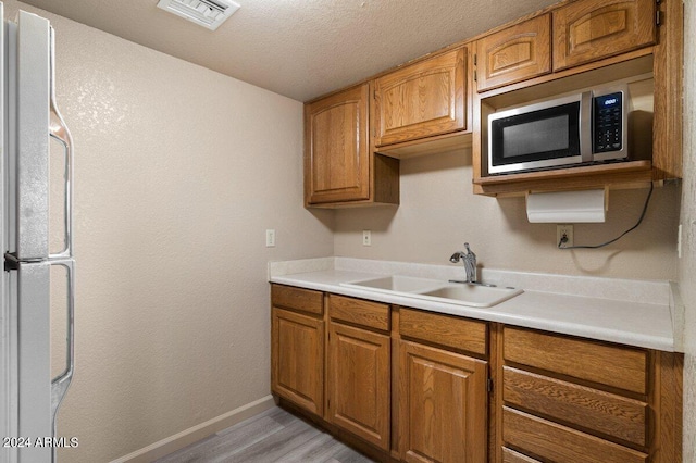 kitchen featuring sink, light hardwood / wood-style floors, a textured ceiling, and white refrigerator