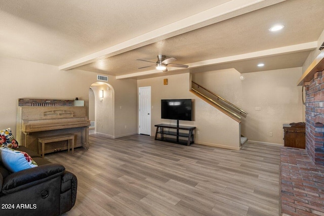 living room featuring ceiling fan, beamed ceiling, wood-type flooring, and a textured ceiling