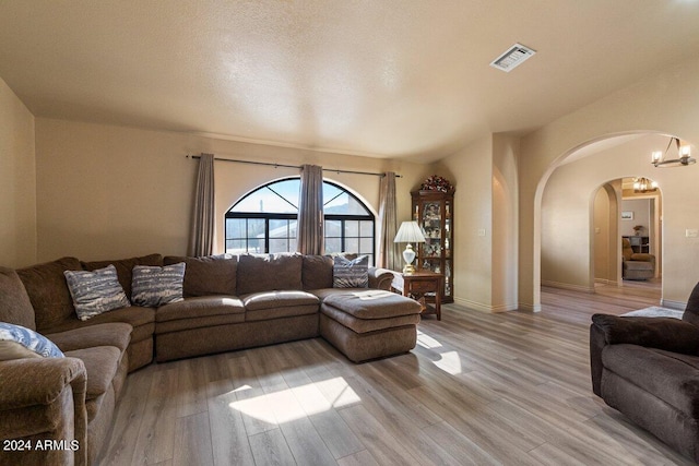 living room with a textured ceiling, a chandelier, light hardwood / wood-style floors, and vaulted ceiling