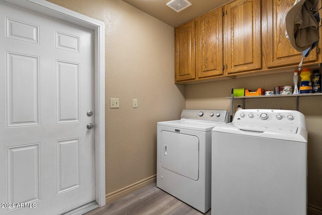 clothes washing area with separate washer and dryer, light hardwood / wood-style flooring, and cabinets