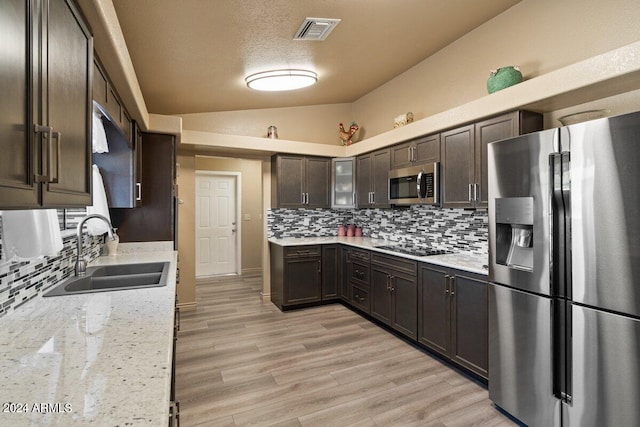 kitchen with sink, stainless steel appliances, light stone counters, light hardwood / wood-style floors, and vaulted ceiling