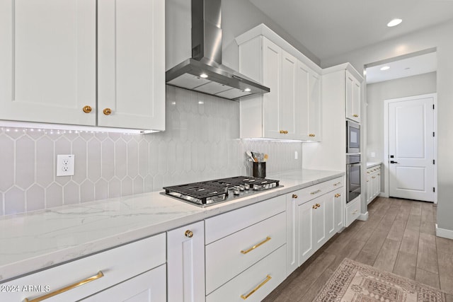 kitchen with decorative backsplash, light stone countertops, appliances with stainless steel finishes, white cabinets, and wall chimney exhaust hood