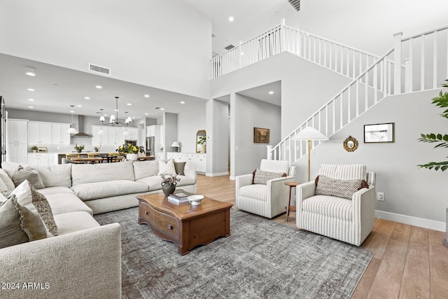 living room with an inviting chandelier, a towering ceiling, and light hardwood / wood-style flooring