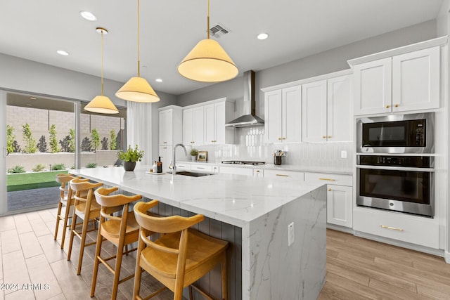 kitchen featuring decorative light fixtures, wall chimney range hood, white cabinets, and stainless steel oven