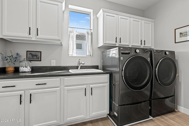 clothes washing area with light hardwood / wood-style floors, sink, washing machine and clothes dryer, and cabinets