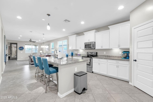 kitchen with white cabinetry, light stone counters, hanging light fixtures, an island with sink, and stainless steel appliances