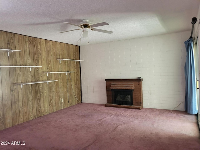 unfurnished living room featuring a textured ceiling, a fireplace, carpet, ceiling fan, and wooden walls