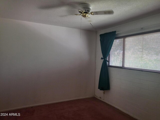 unfurnished room with a textured ceiling, brick wall, ceiling fan, and carpet