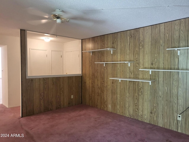 interior space with a textured ceiling, dark carpet, and wood walls