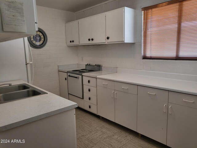 kitchen featuring tile walls, electric range oven, sink, and white cabinetry