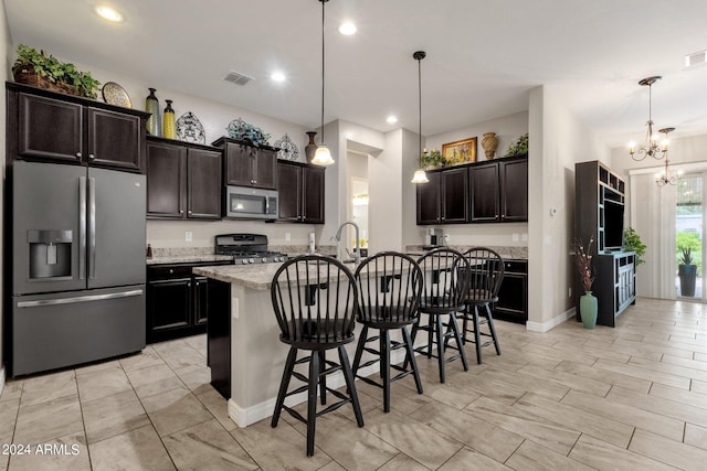 kitchen with an island with sink, appliances with stainless steel finishes, pendant lighting, and a kitchen bar