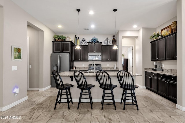 kitchen featuring appliances with stainless steel finishes, a breakfast bar, decorative light fixtures, a kitchen island with sink, and dark brown cabinetry