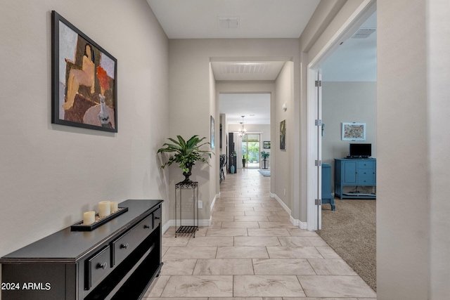 hallway featuring an inviting chandelier and light carpet