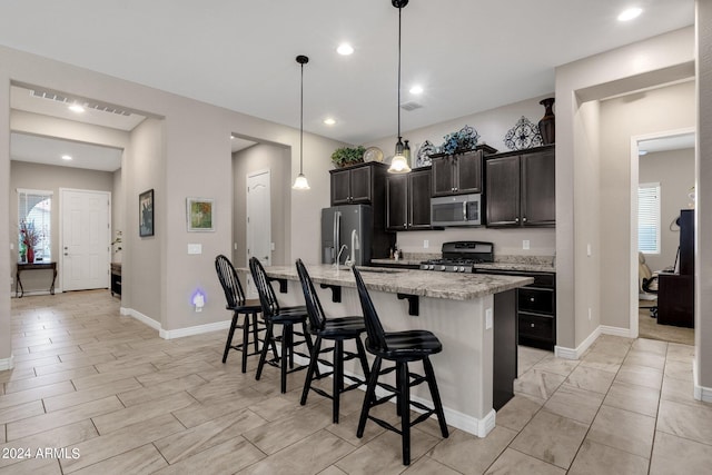 kitchen with appliances with stainless steel finishes, a kitchen island with sink, hanging light fixtures, light stone counters, and a kitchen bar