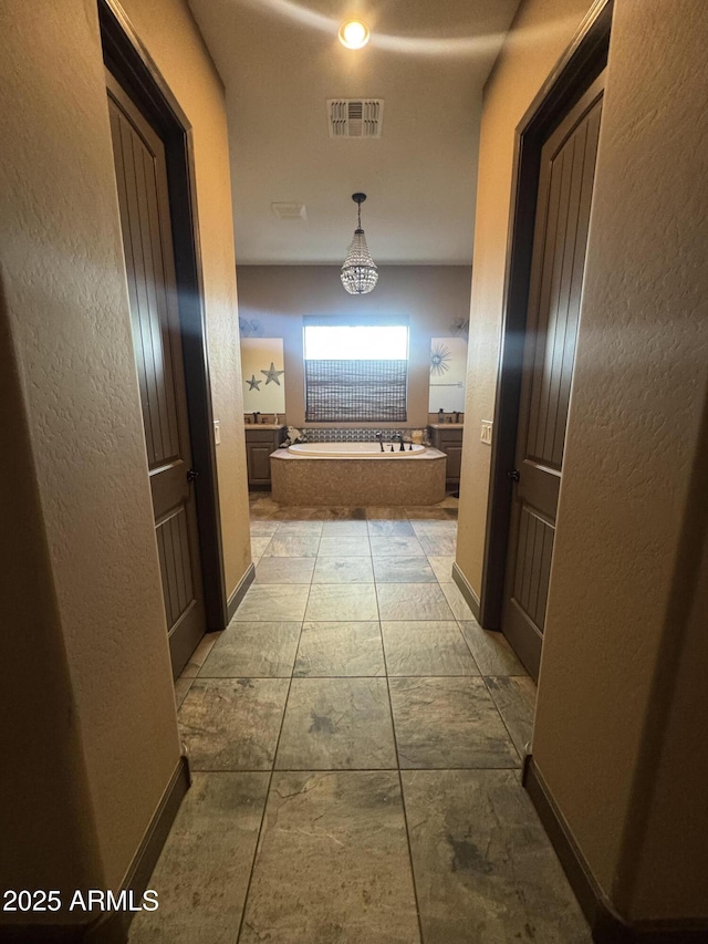 hall with a textured wall, visible vents, and baseboards