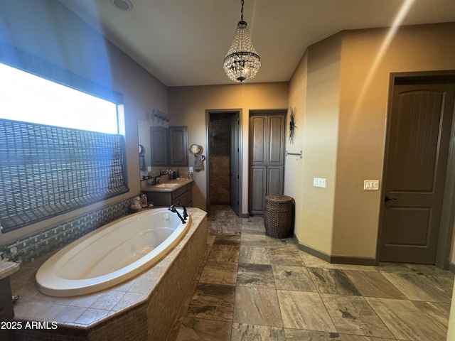bathroom featuring a garden tub, an inviting chandelier, vanity, baseboards, and stone finish flooring