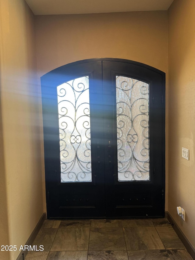 foyer entrance with arched walkways, baseboards, and french doors
